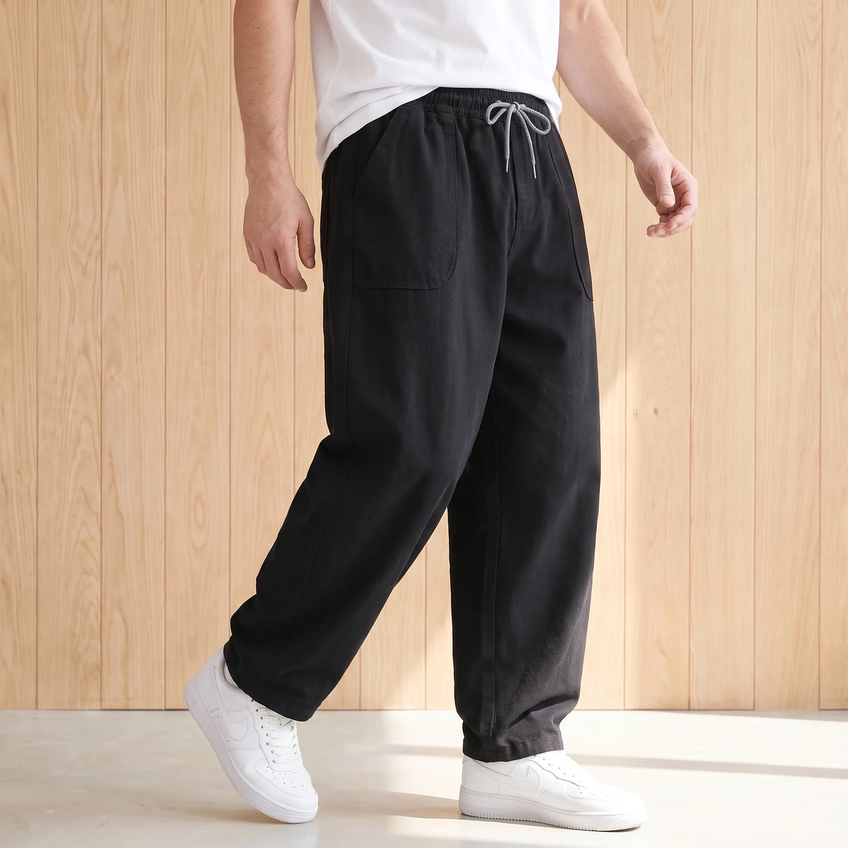 Man walking in the black barrel leg trousers with a white tee and white sneakers