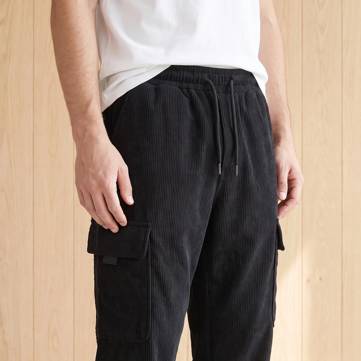 Man wearing black corduroy cargo joggers with a plain white tee, hand near the side pocket