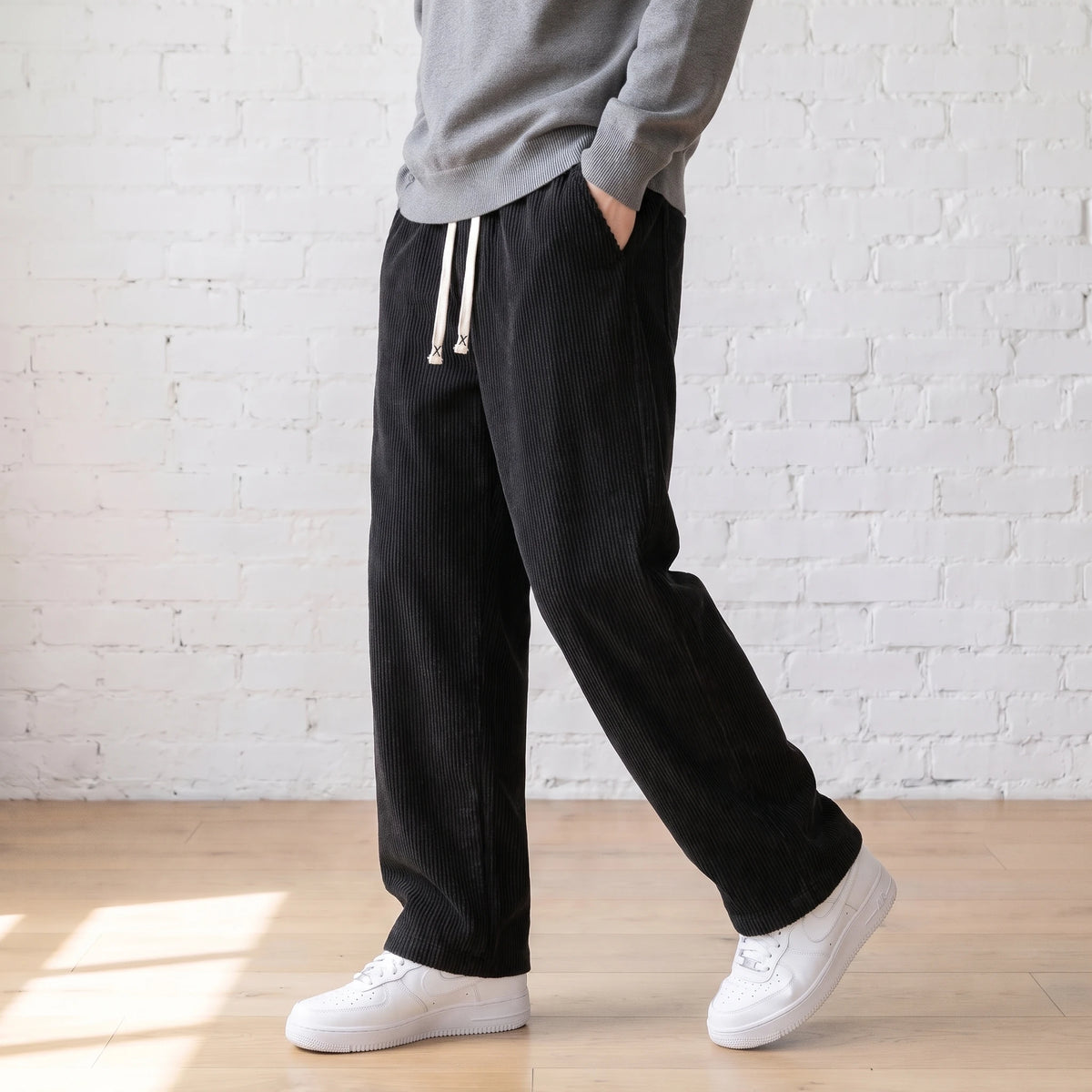 Man walking in the black wide corduroy trousers with a grey sweater and white sneakers