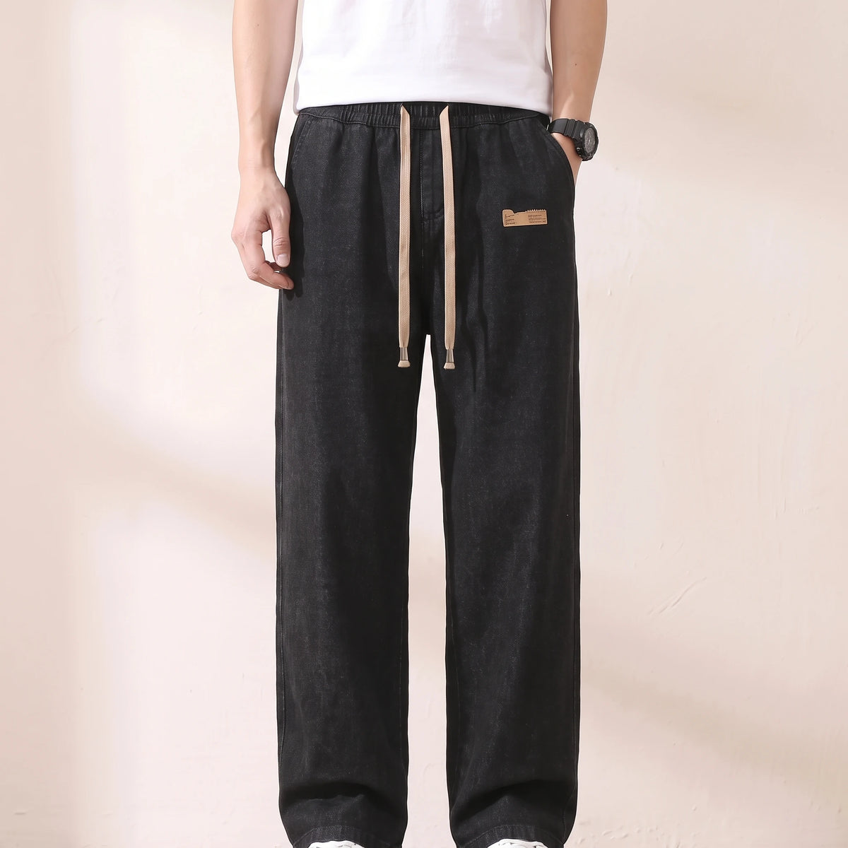 Man wearing black baggy drawstring jeans with a plain white tee, hand at his hip