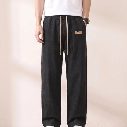 Man wearing black baggy drawstring jeans with a plain white tee, hand at his hip