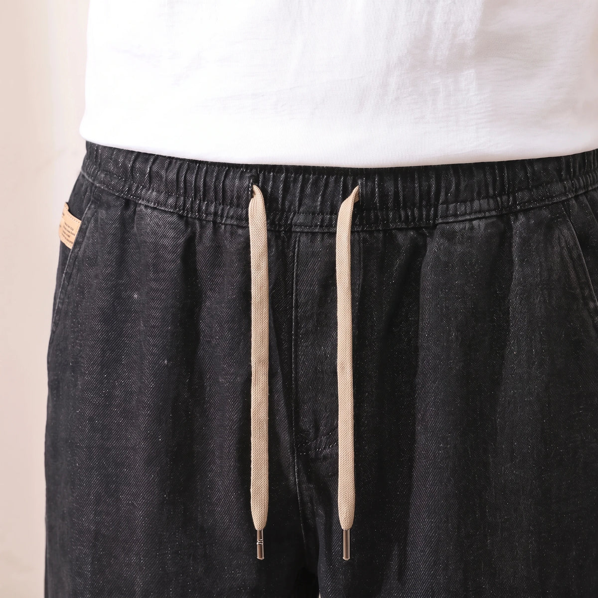 Close-up of the elastic drawstring waist and long beige cords on black baggy jeans