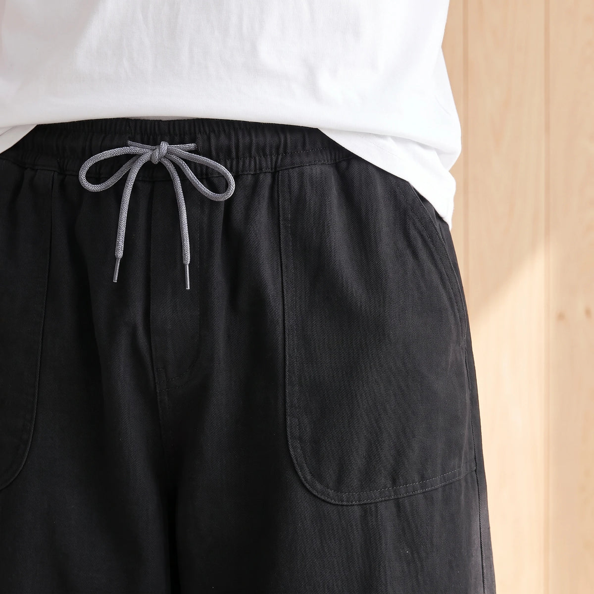 Close-up of the elastic waistband, grey drawstring and large patch pocket on the black trousers