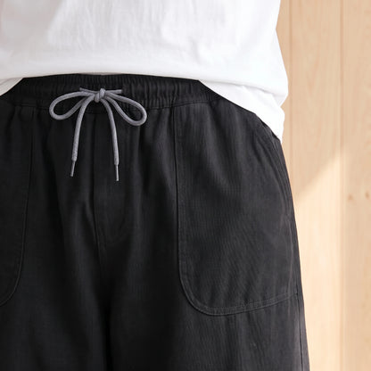 Close-up of the elastic waistband, grey drawstring and large patch pocket on the black trousers