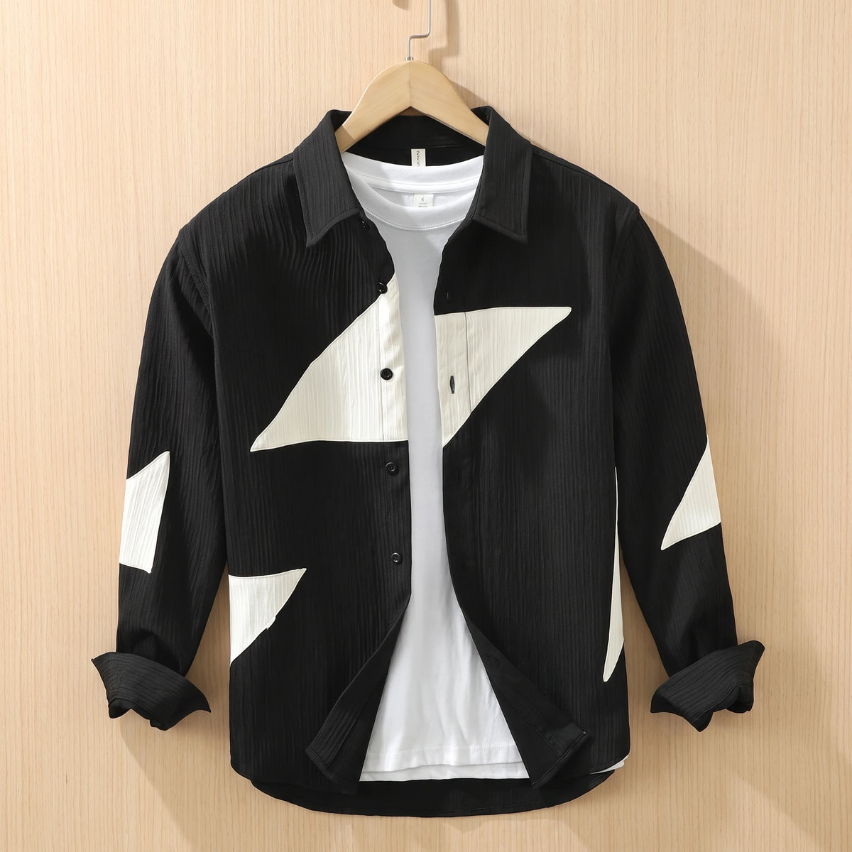 Black textured shirt with large cream contrast panels hanging on a wooden hanger