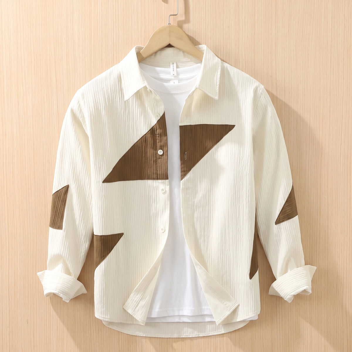 Beige textured shirt with brown contrast panels hanging on a wooden hanger