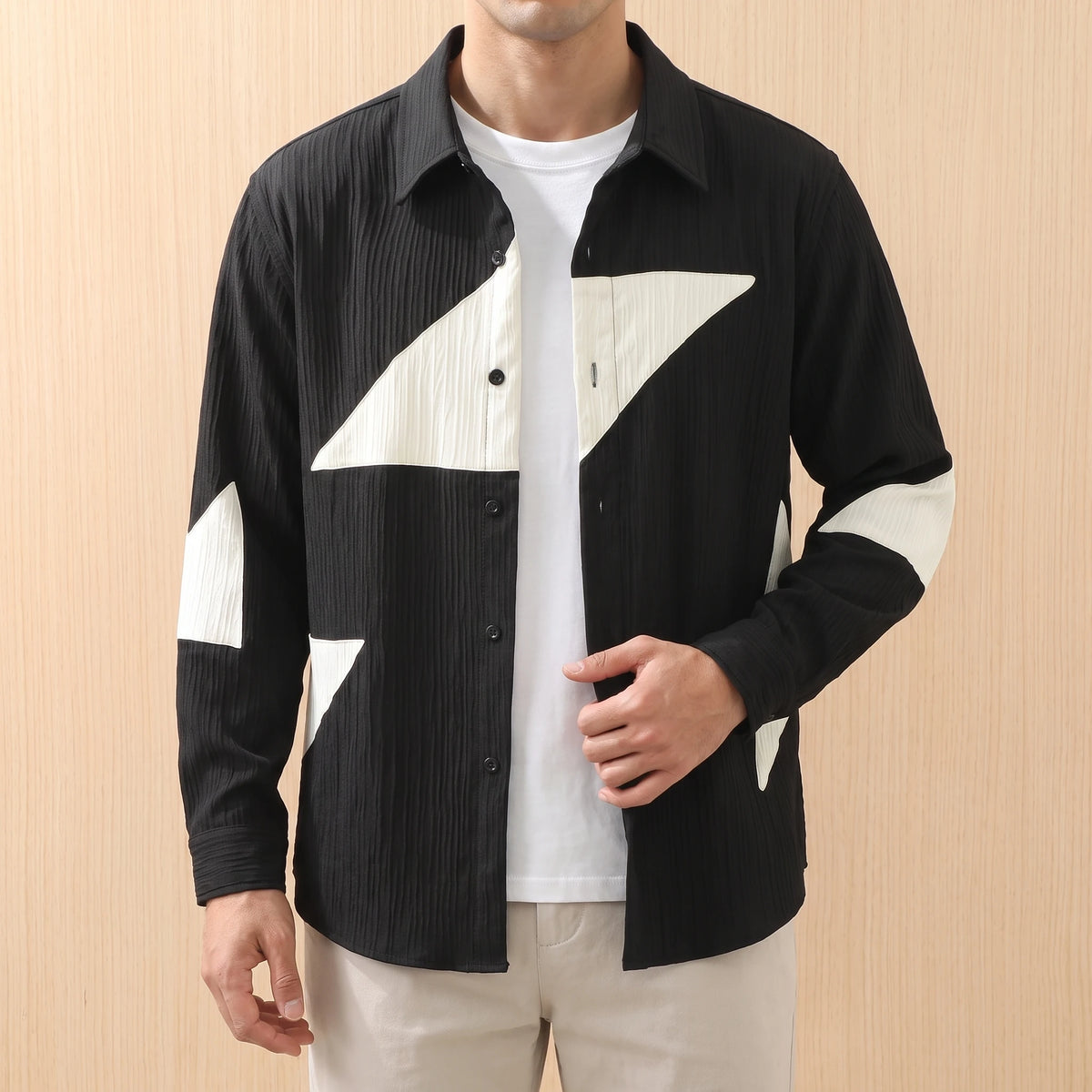 Man wearing a black panelled shirt open over a white tee with stone chinos