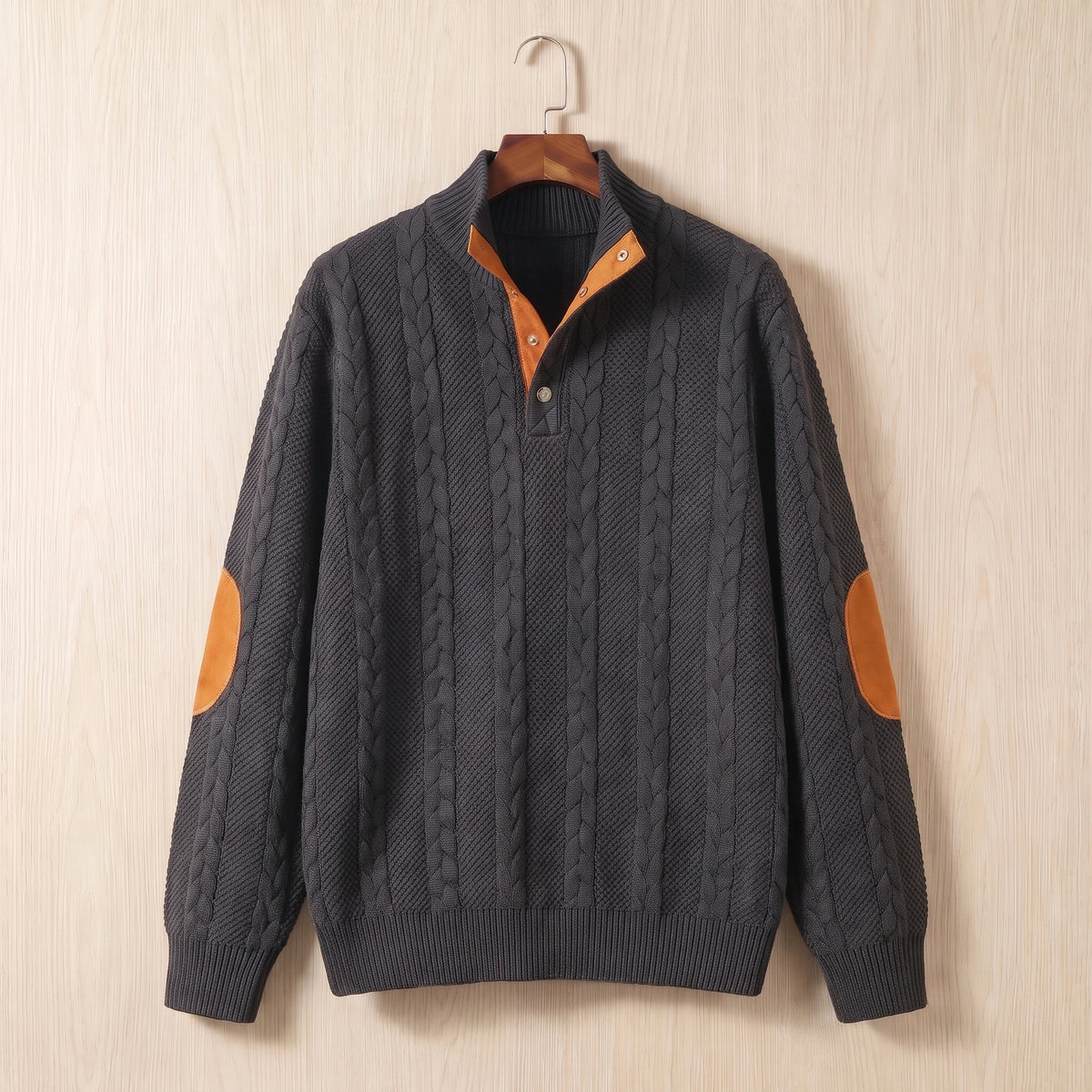 Dark grey cable knit sweater with a stand collar, button neck and tan elbow patches hanging on a wooden hanger