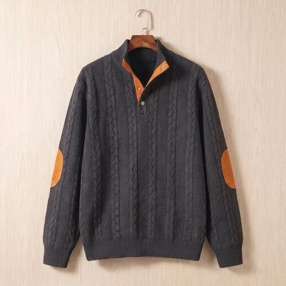 Dark grey cable knit sweater with a stand collar, button neck and tan elbow patches hanging on a wooden hanger