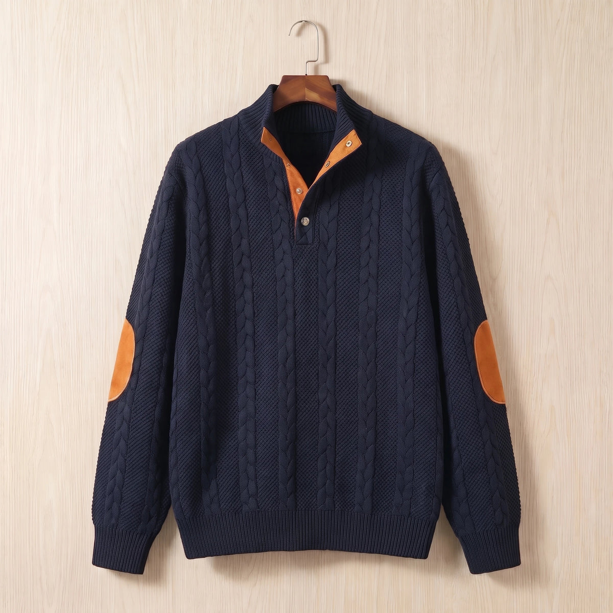 Navy blue cable knit sweater with a stand collar, button neck and tan elbow patches hanging on a wooden hanger
