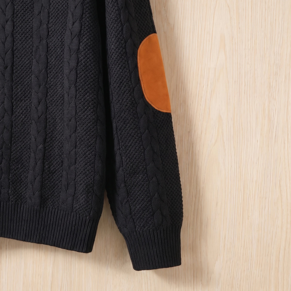 Close-up of the tan elbow patch, cable knit and ribbed cuff on the black sweater sleeve