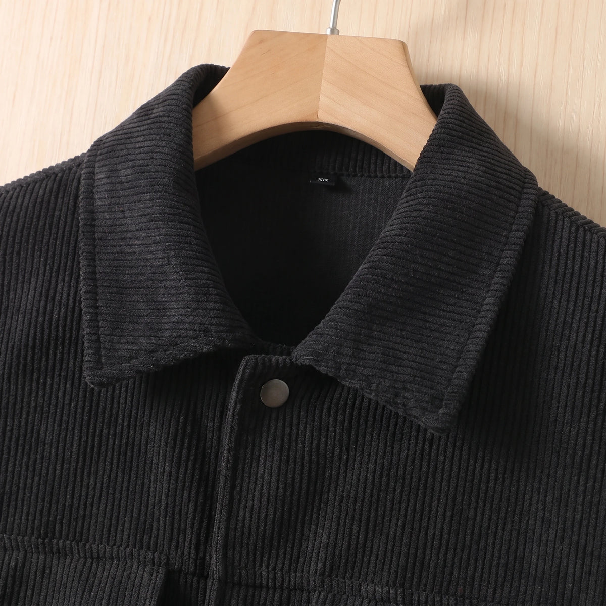 Close-up of the spread collar and snap placket on the black corduroy jacket