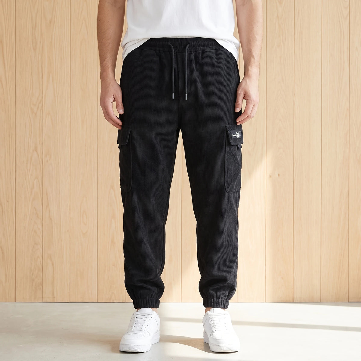 Black corduroy cargo joggers with a drawcord waist and large side pocket worn with white sneakers