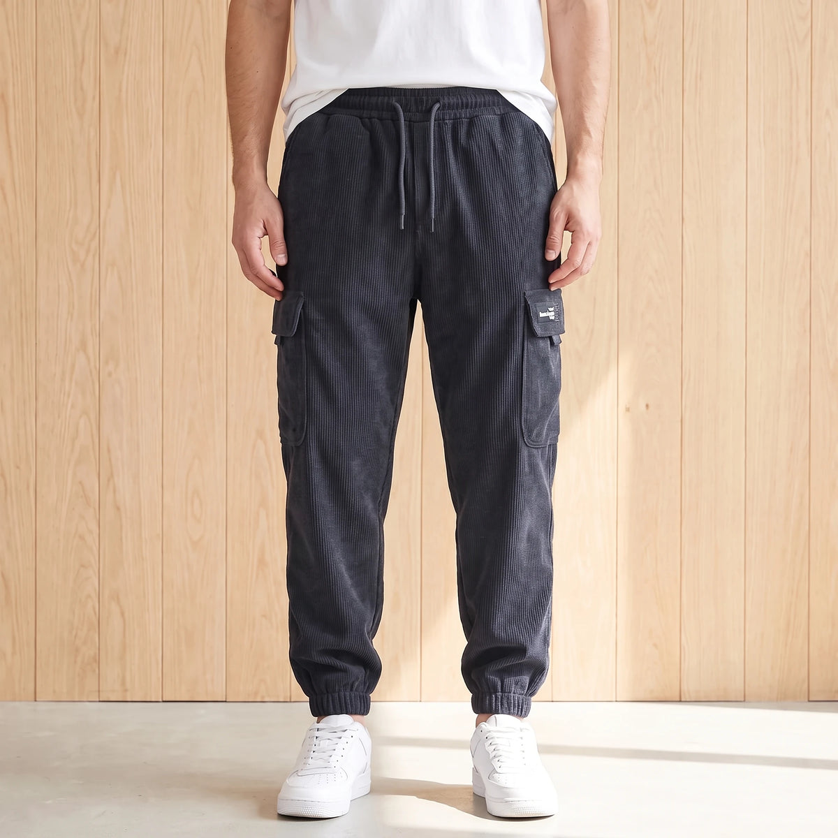 Gray corduroy cargo joggers with a drawcord waist and large side pocket worn with white sneakers