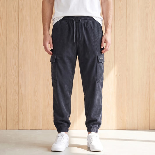 Gray corduroy cargo joggers with a drawcord waist and large side pocket worn with white sneakers