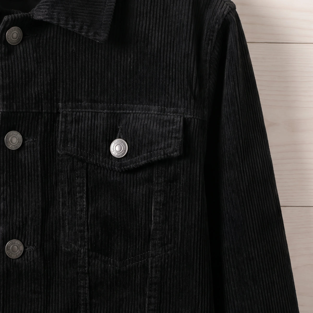 Close-up of the chest flap pocket and metal button on the black corduroy trucker jacket