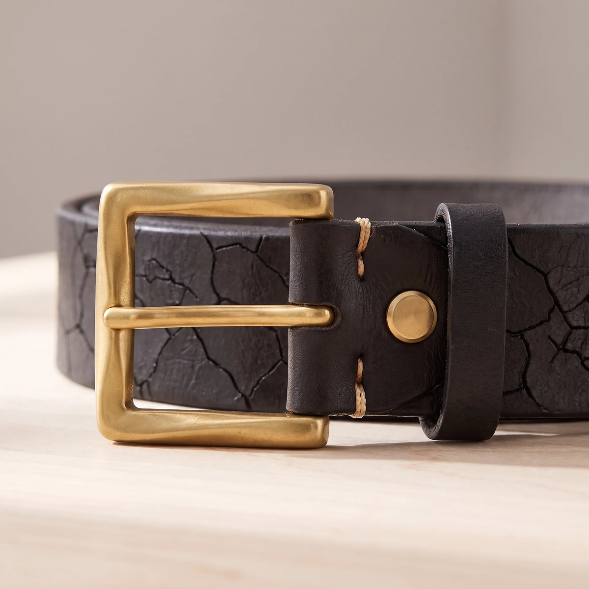 Close-up of the brass buckle, rivet and keeper on the black cracked leather belt
