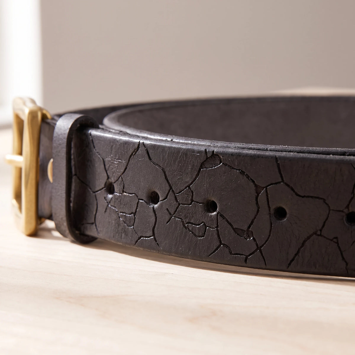 Close-up of the cracked leather pattern and holes on the black belt strap