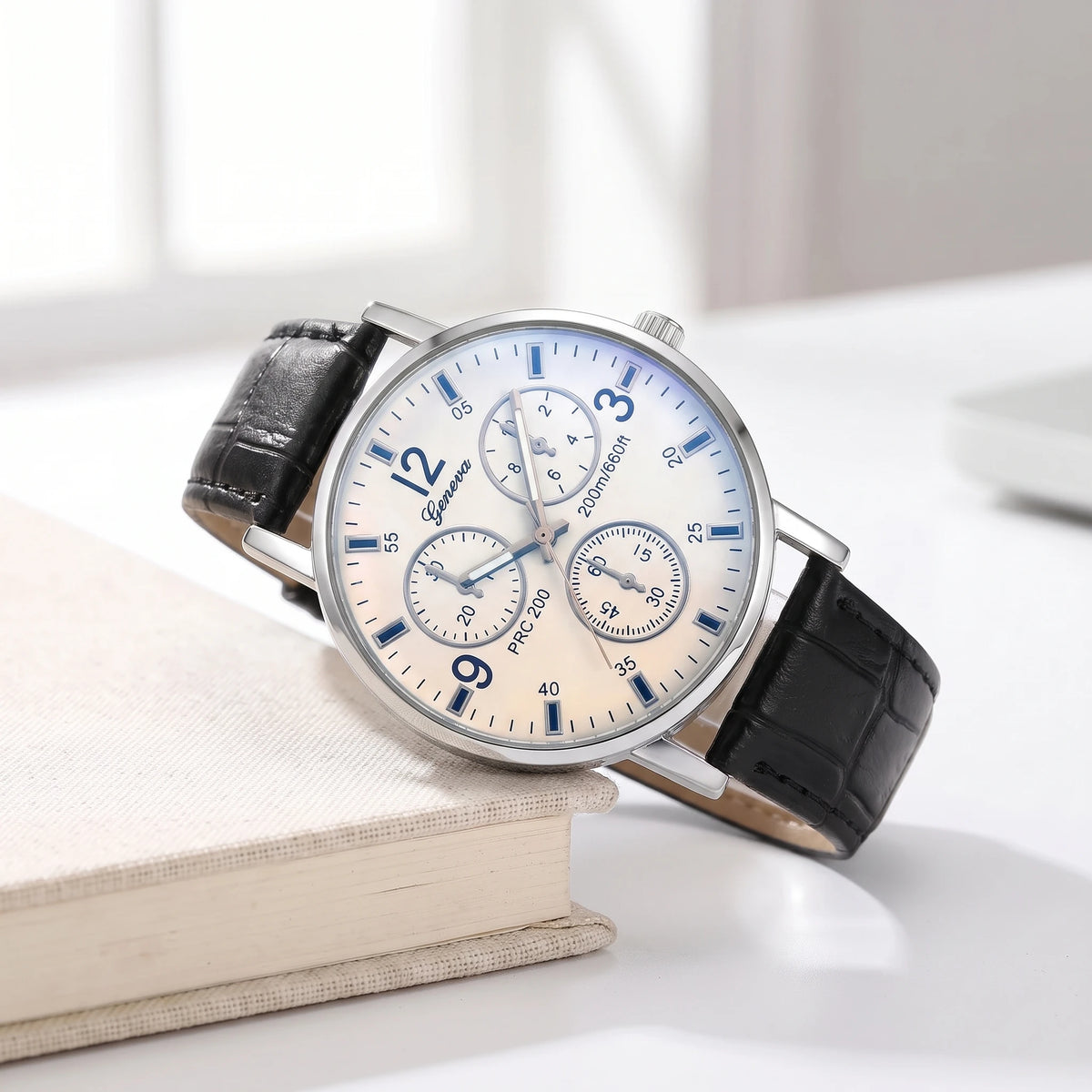 White dial quartz watch with a black croc-grain strap resting on a cream book