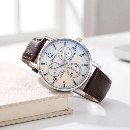 White dial quartz watch with a brown croc-grain strap resting on a cream book