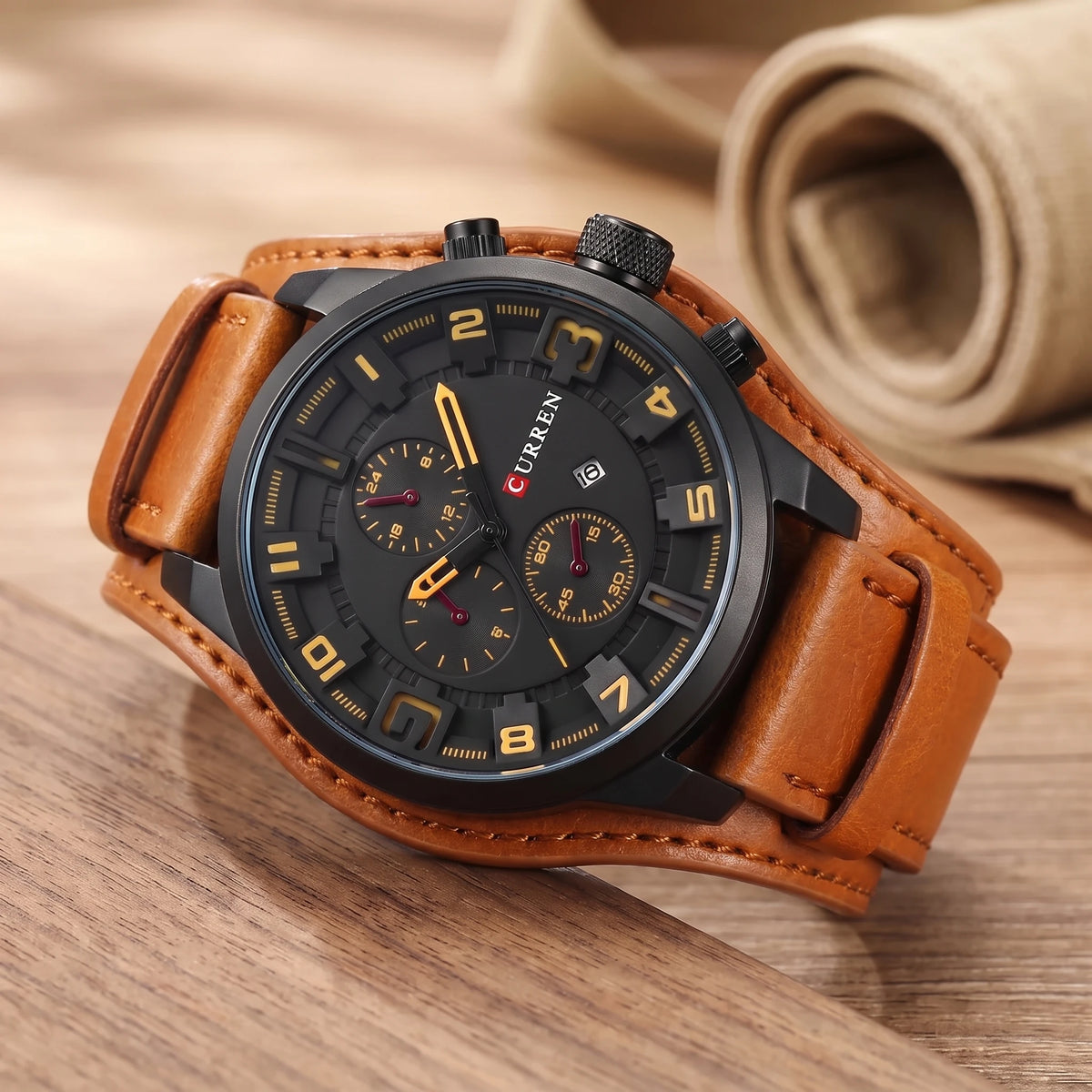 Black dial watch with yellow numerals and a wide tan leather cuff strap on a walnut table