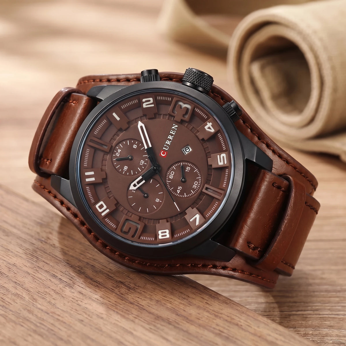 Brown dial watch with a wide brown leather cuff strap on a walnut table
