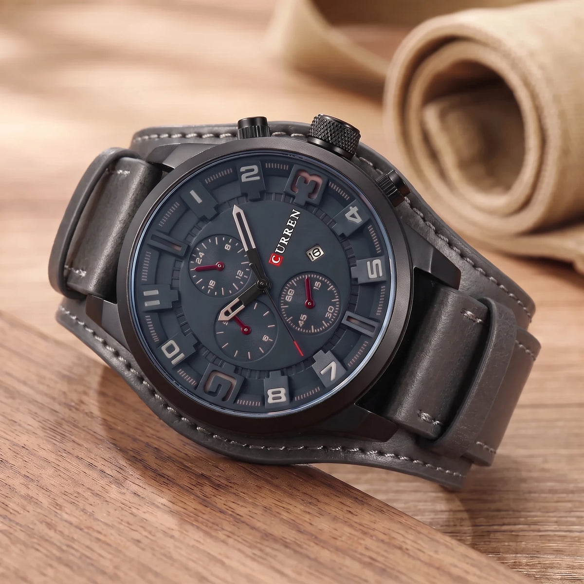 Grey dial watch with a wide grey leather cuff strap on a walnut table