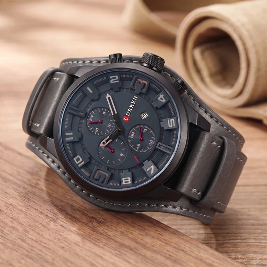 Grey dial watch with a wide grey leather cuff strap on a walnut table