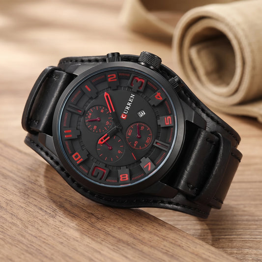 Black watch with red numerals and a wide black leather cuff strap on a walnut table
