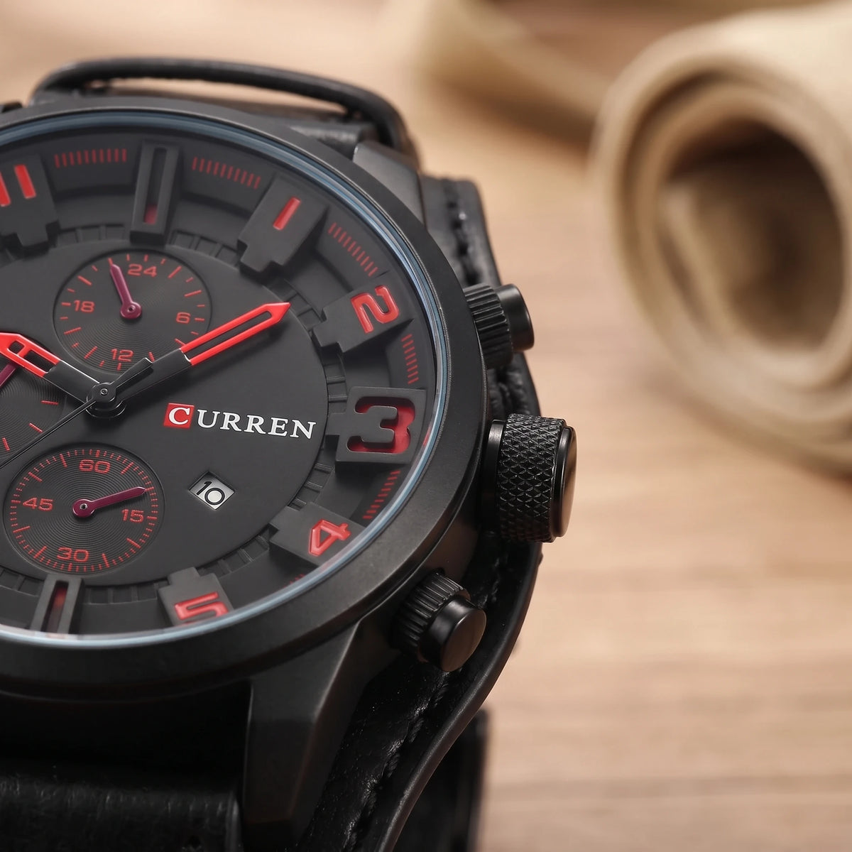 Close-up of the dial edge, date window and knurled crown on a black cuff strap watch