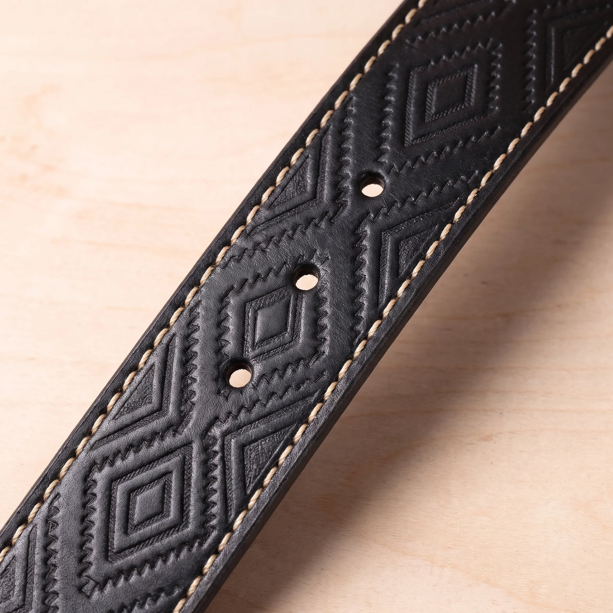 Close-up of the embossed diamond strap and punched holes on the black leather belt