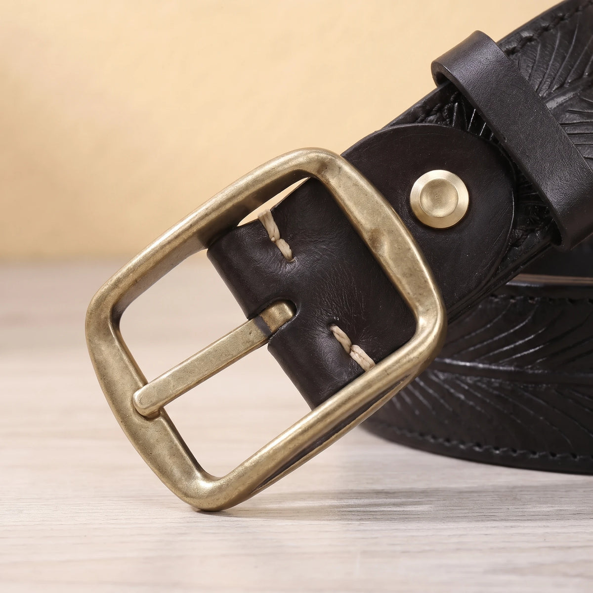 Close-up of the brass pin buckle and keeper on the black feather embossed leather belt