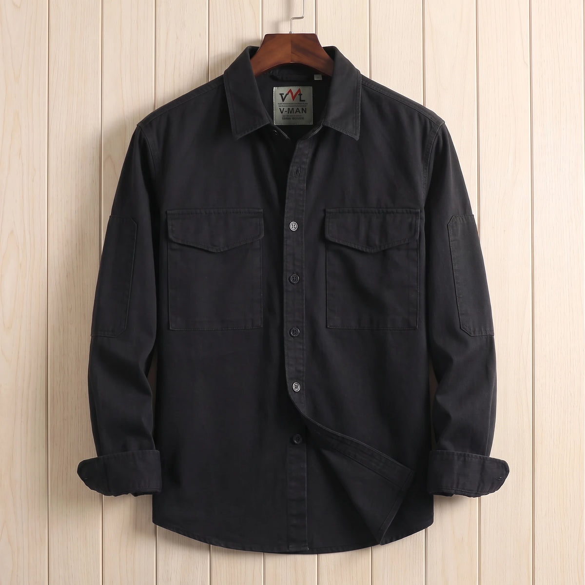Black heavy cotton overshirt with two flap chest pockets hanging on a wooden hanger