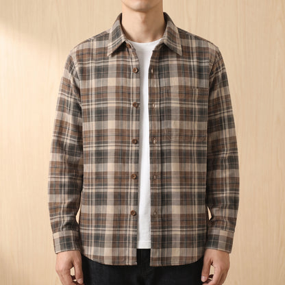 Man wearing a khaki brown plaid shirt open over a white tee