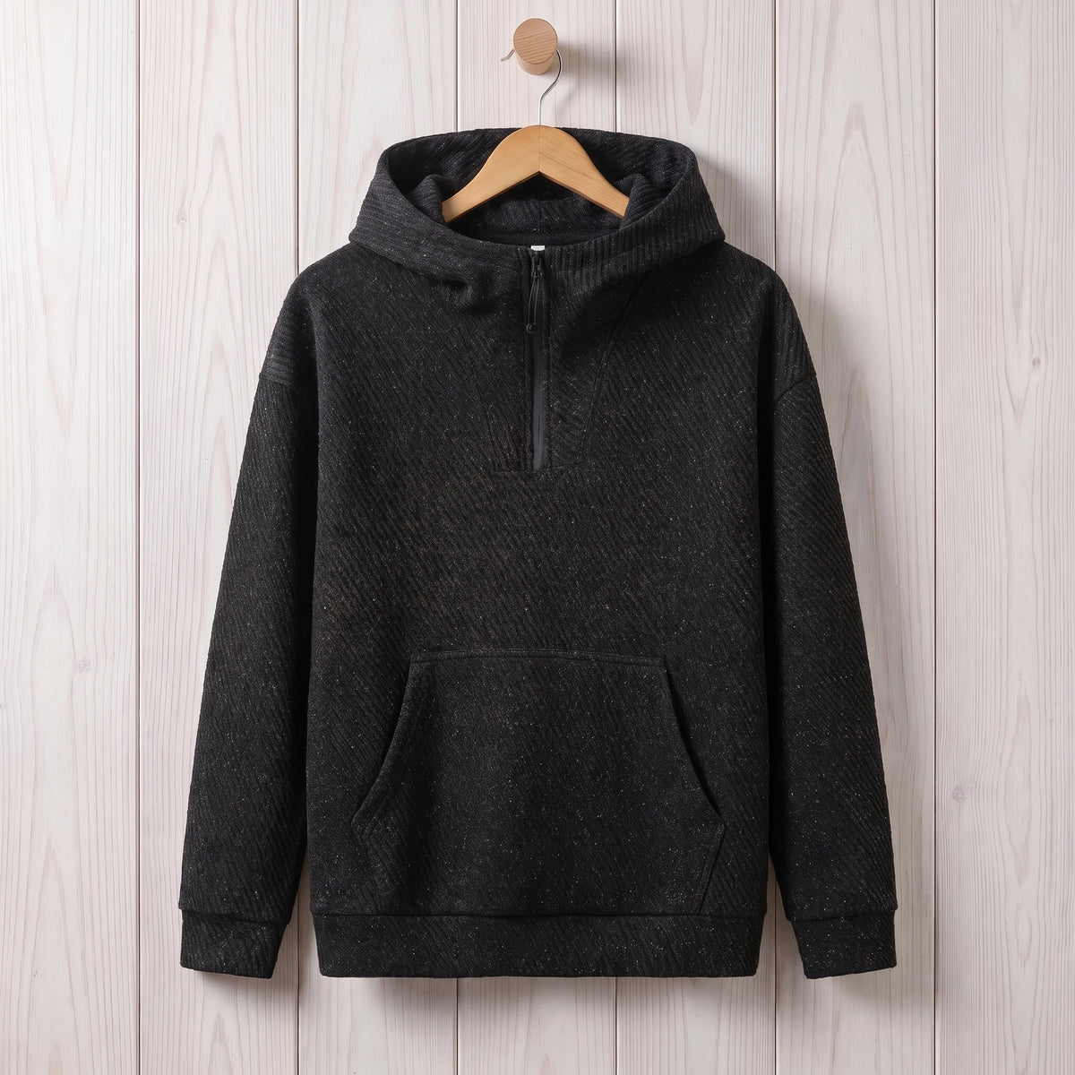 Black loose hooded sweater with a short zip and kangaroo pocket hanging on a wooden hanger