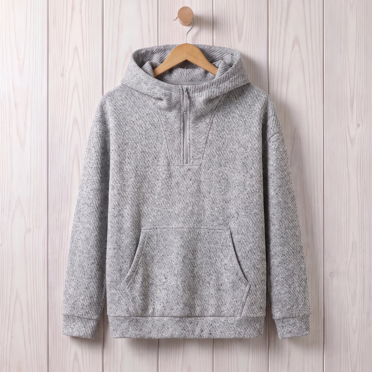 Light grey loose hooded sweater with a short zip and kangaroo pocket hanging on a wooden hanger