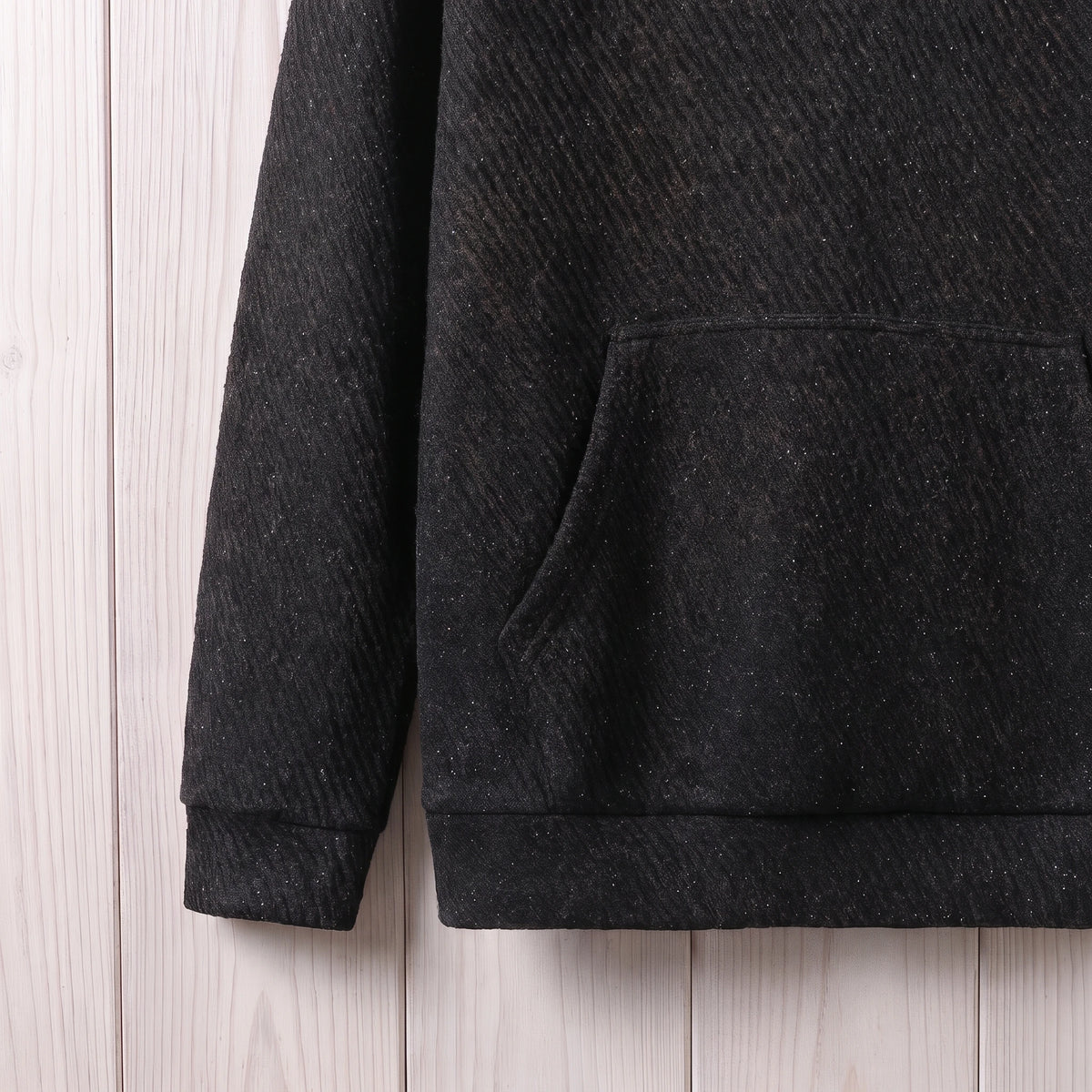 Close-up of the kangaroo pocket, ribbed cuff and hem on the black hooded sweater