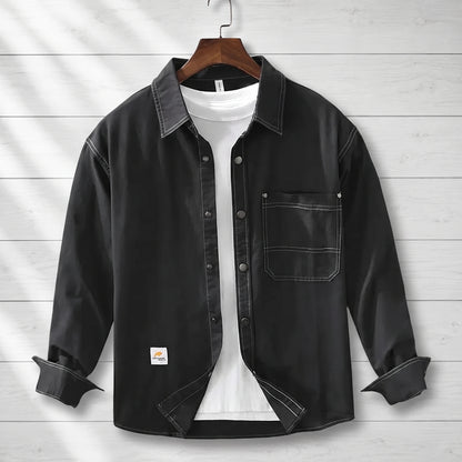 Black loose workwear shirt with contrast stitching and a patch chest pocket hanging on a wooden hanger