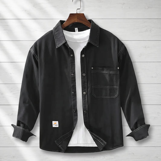 Black loose workwear shirt with contrast stitching and a patch chest pocket hanging on a wooden hanger