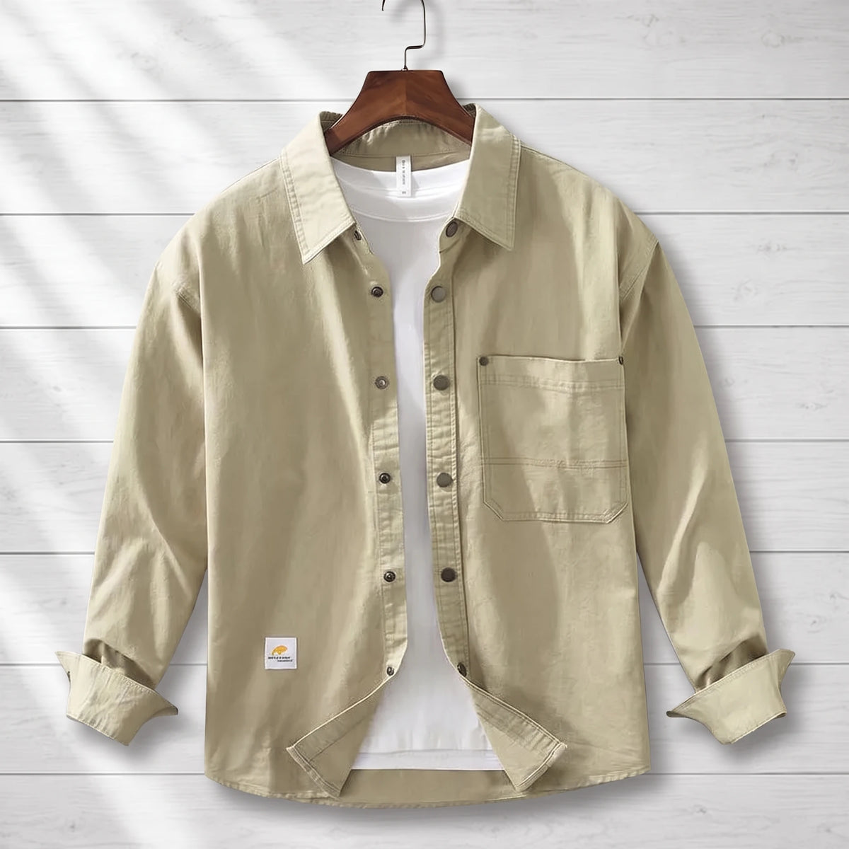 Khaki loose workwear shirt with a patch chest pocket hanging on a wooden hanger