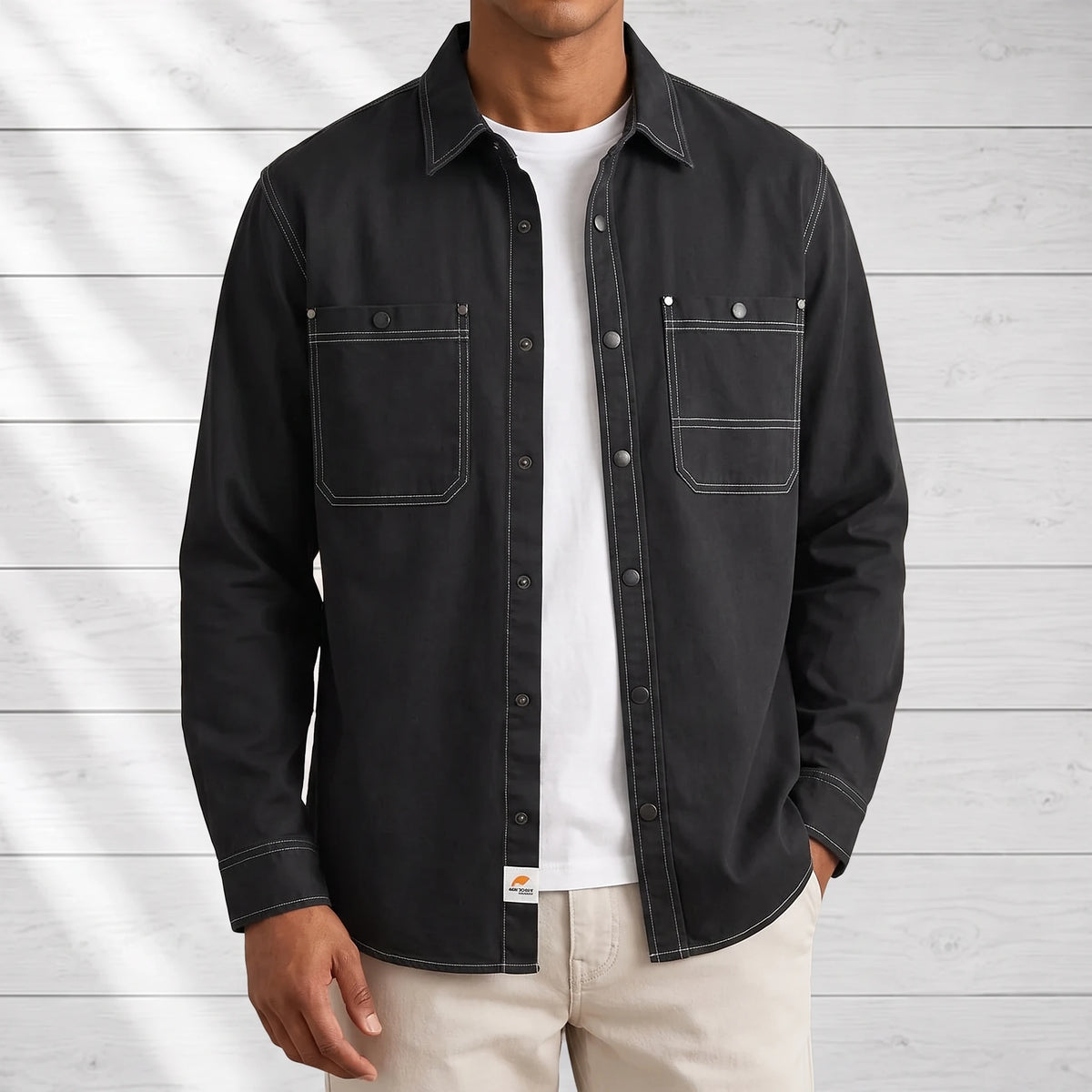 Man wearing a black workwear shirt open over a white tee with stone chinos