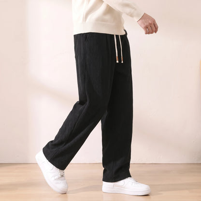 Man walking in the black pleated corduroy trousers with a cream sweater and white sneakers