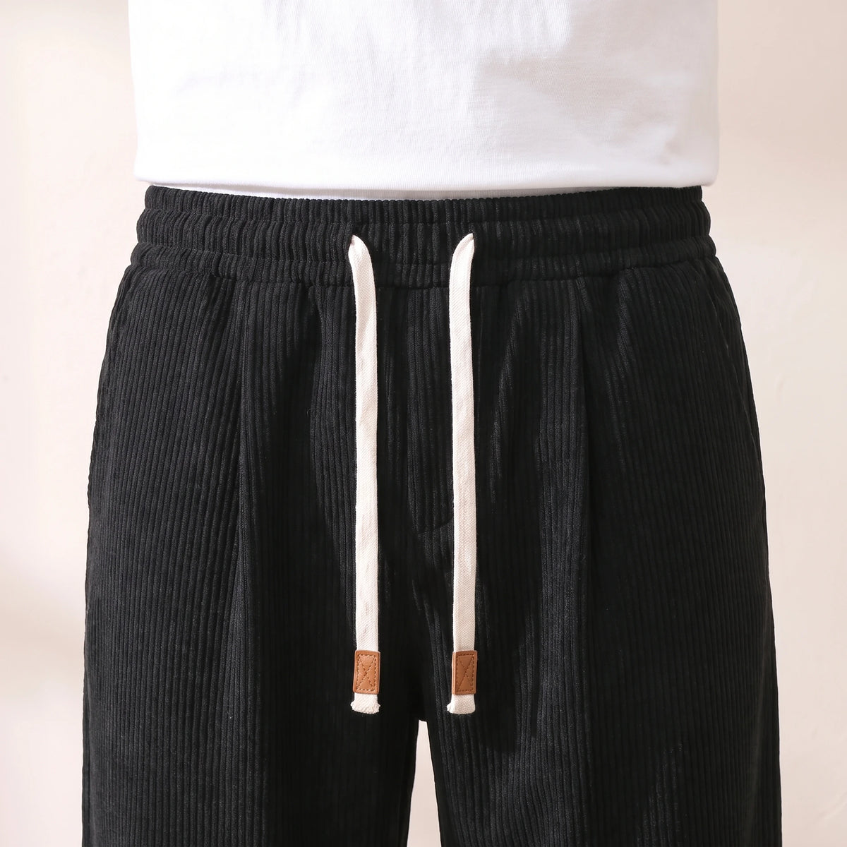 Close-up of the pleated waistband, white drawstring and tan cord tags on the black corduroy trousers