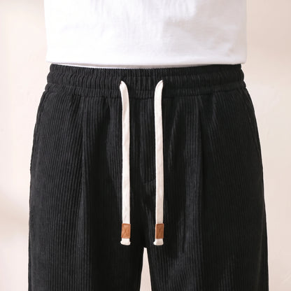 Close-up of the pleated waistband, white drawstring and tan cord tags on the black corduroy trousers