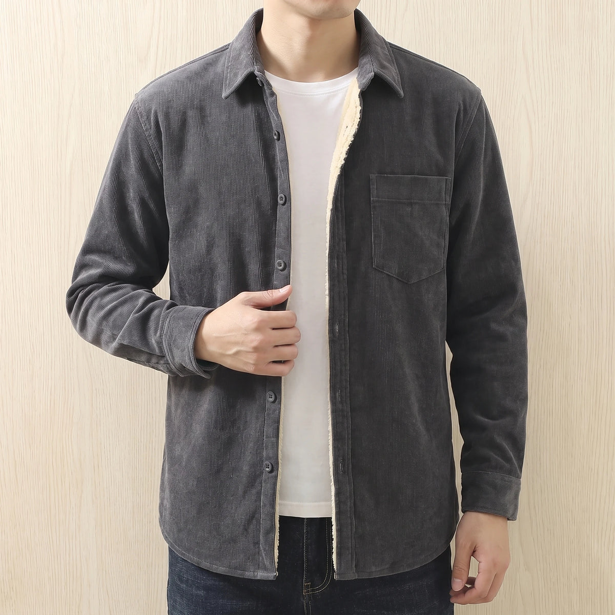 Man wearing a grey fleece lined corduroy shirt open over a white tee with dark jeans