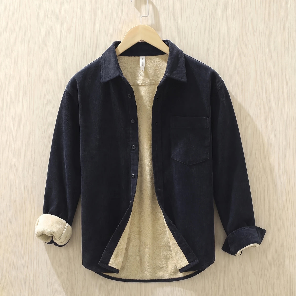 Navy fleece lined corduroy shirt with a chest pocket hanging on a wooden hanger