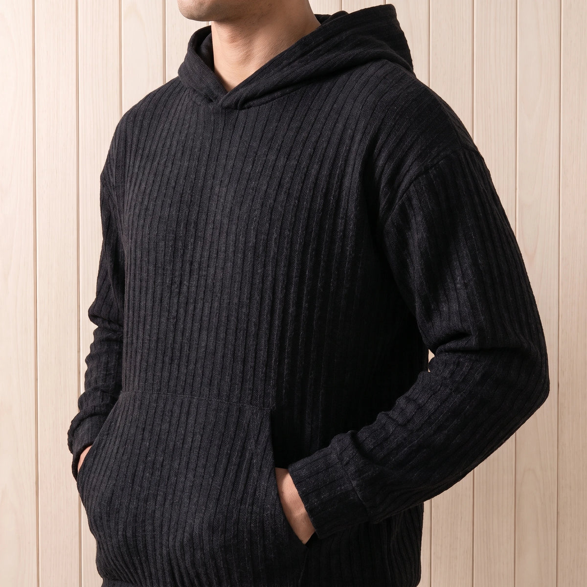 Man wearing the black ribbed knit hooded sweater with hands in the front pocket