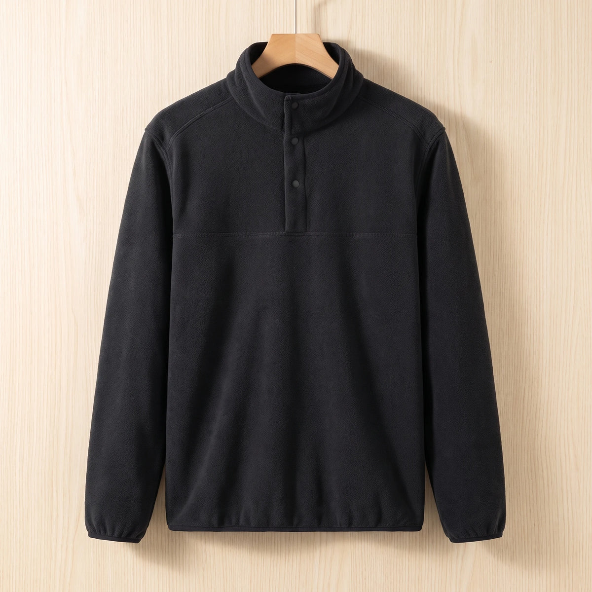 Black fleece pullover with a snap collar and elastic cuffs hanging on a wooden hanger