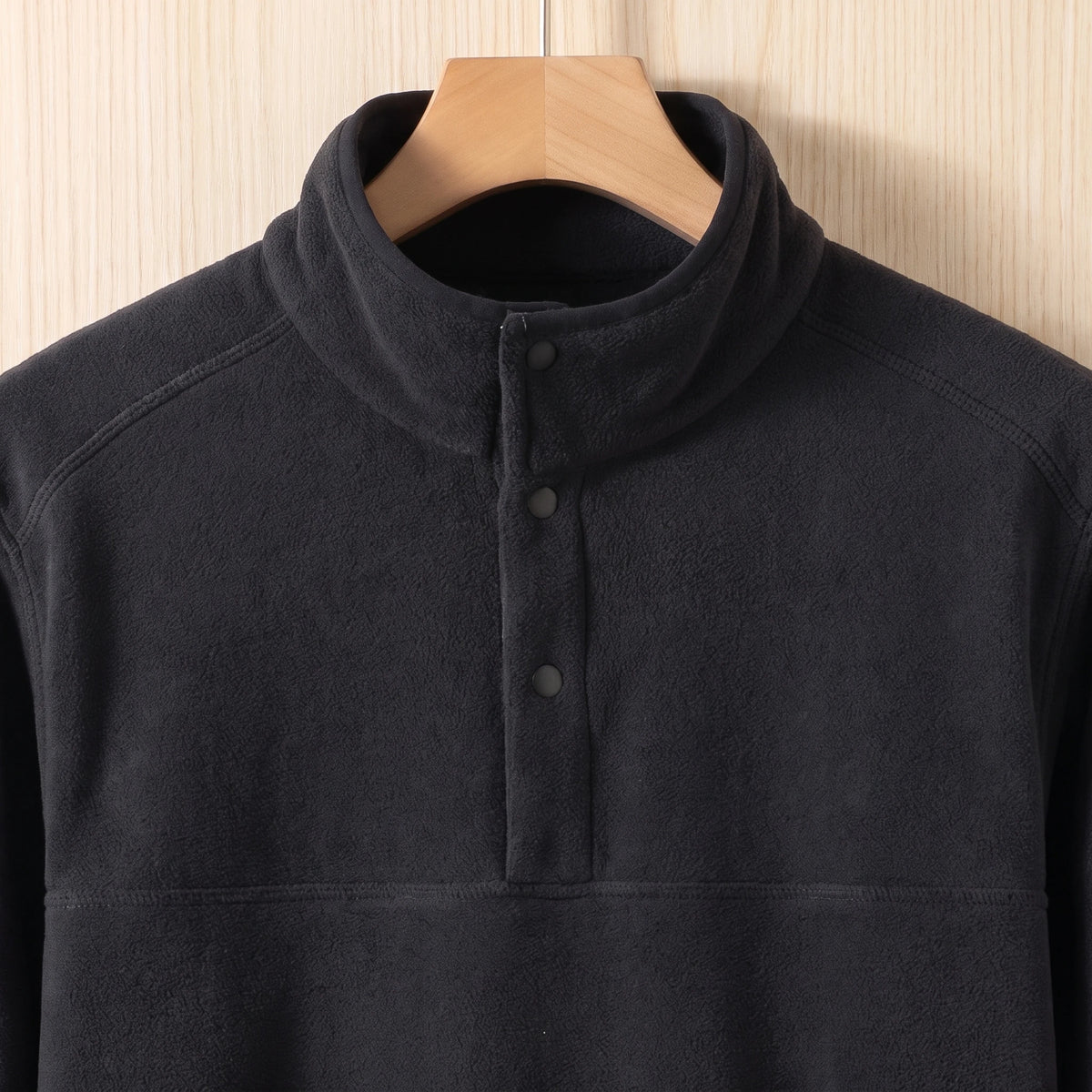 Close-up of the stand collar and three snap buttons on a black fleece pullover