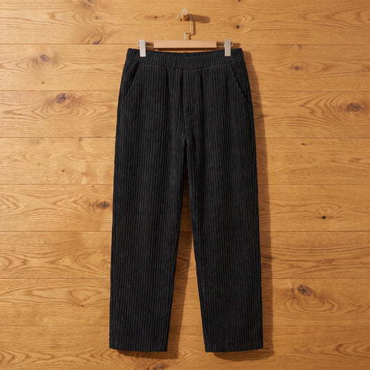 Black thick rib corduroy trousers hanging on an oak wall